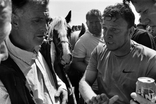 An up close photo of two men engaged in negotiation. The horse they are negotiating over can be seen in the background