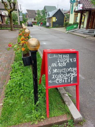 A blackboard sign with a red border on a roadside. The sign is in Ukrainian.