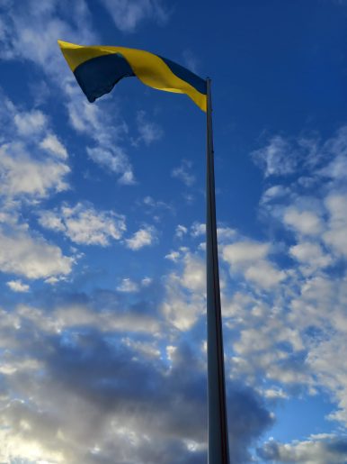 The Ukrainian flag, blue above and white below, viewed from the bottom of the flagpole. The sky is blue with small clouds