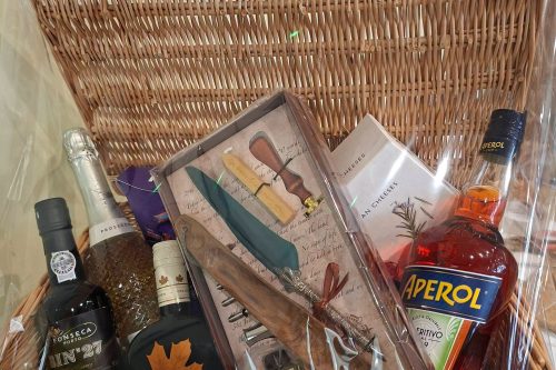 A photo of a raffle prize basket including several bottles of wine, a bottle of Aperol, and a quill and ink set