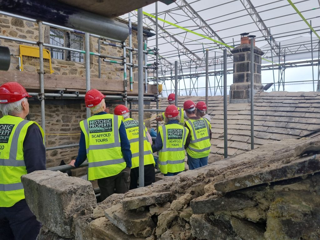 A group of men and women in hi-vis jackets and hard hats stand on a scaffolding platform inspecting a newly repaired chimney 