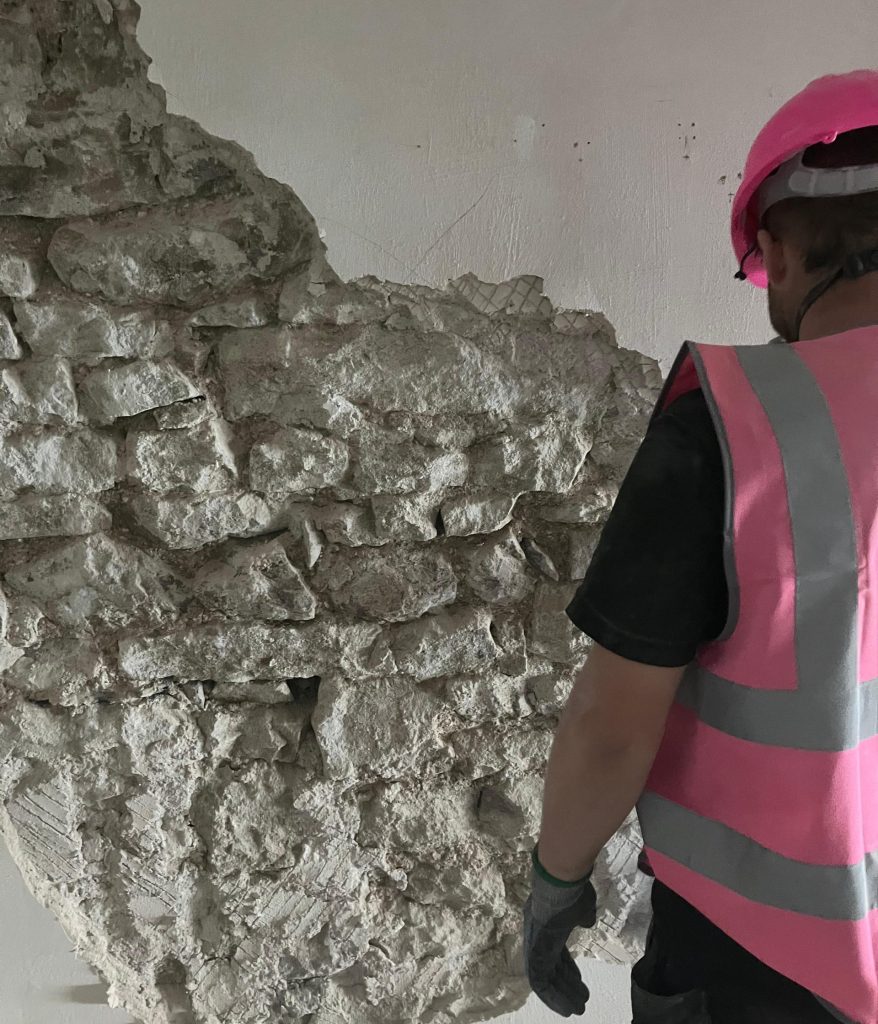 Plasterer at work knocking off gypsum plaster to reveal stone wall beneath