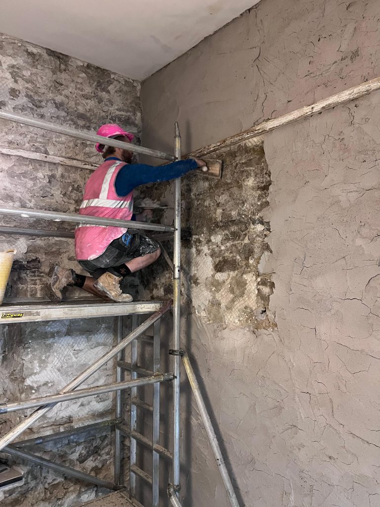 Plasterer applying a first coat of lime plaster to an internal stone wall
